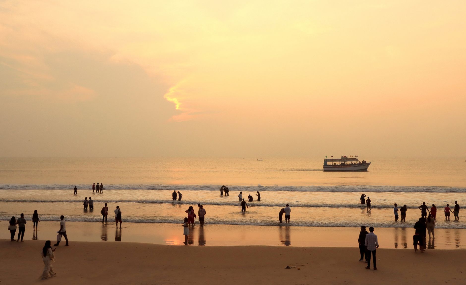A serene beach scene in Pondicherry, India, at sunset with people enjoying the shoreline and a boat in the distance.