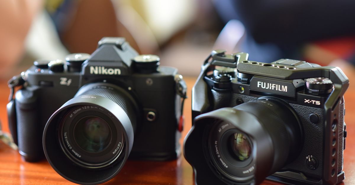 Close-up of Nikon and Fujifilm cameras on a wooden table, focusing on lens details.