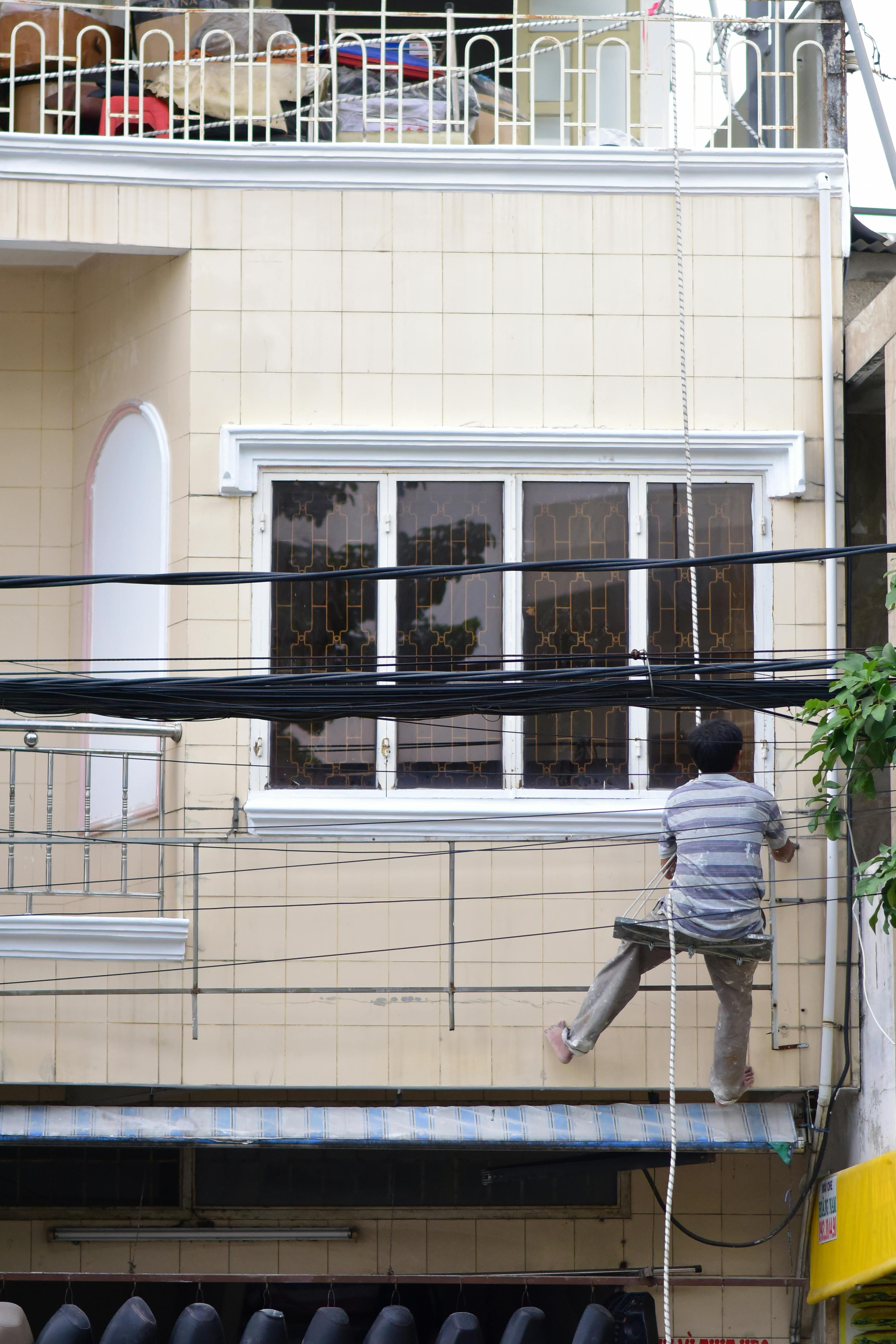 Worker hanging on facade, painting outdoors with safety gear in urban setting.