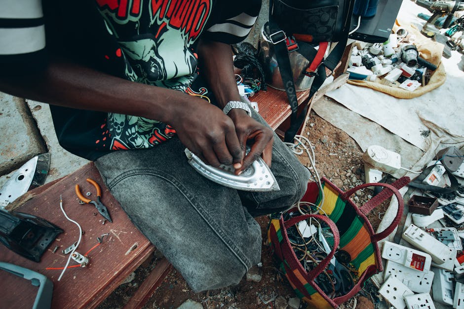 A person skillfully repairs electronics outdoors in Kaduna, Nigeria, showcasing local craftsmanship and resourcefulness.