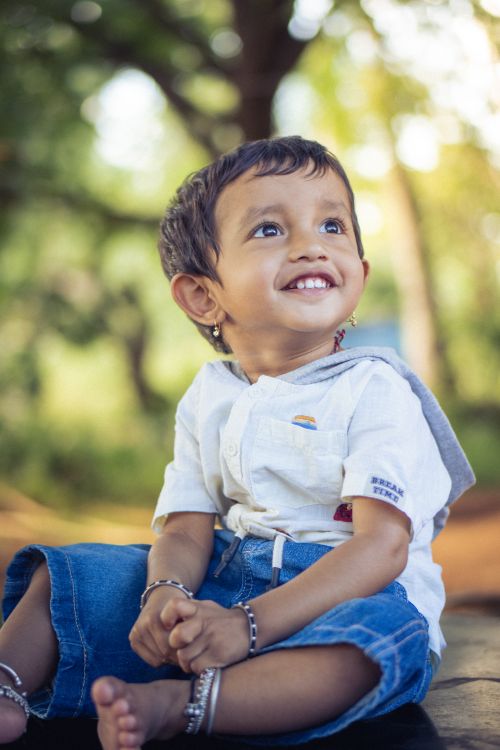 Free Joyful child sitting outdoors on a sunny day with trees in the background. Stock Photo