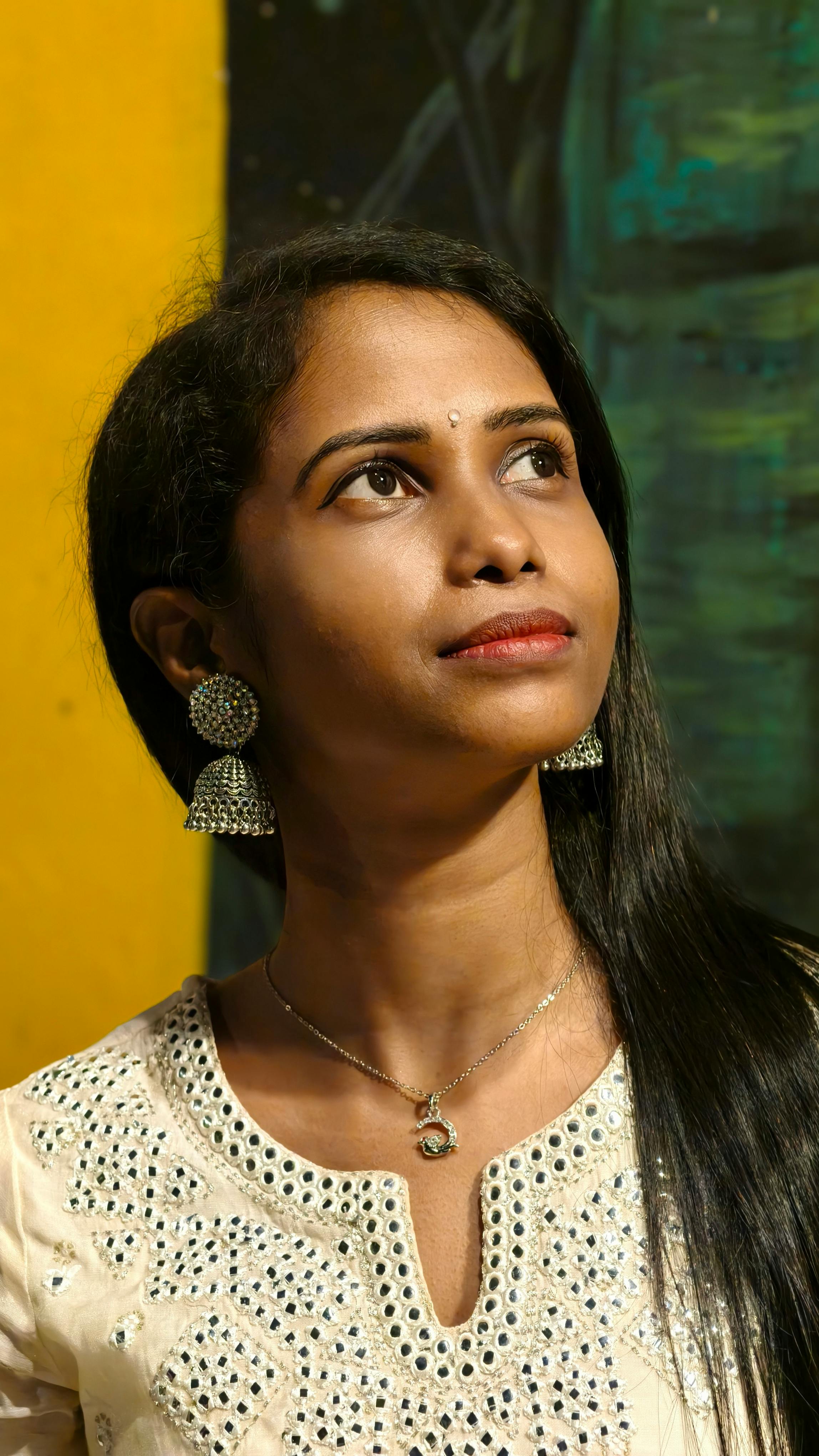 A thoughtful woman in traditional attire with jhumkas, highlighted by vibrant colors and artistic background.