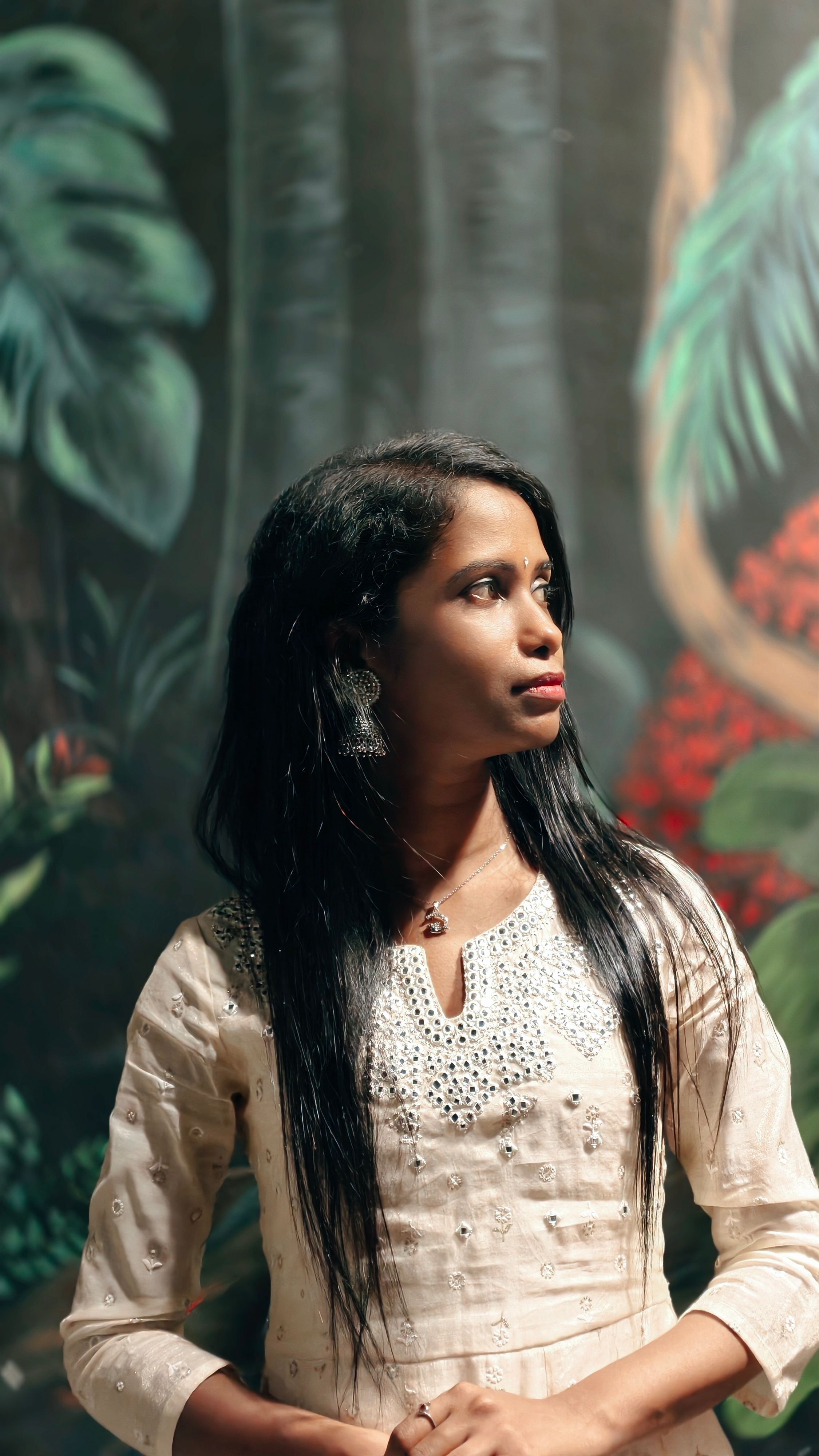 Portrait of a woman in traditional Indian attire against a mural backdrop, exuding elegance and thoughtfulness.