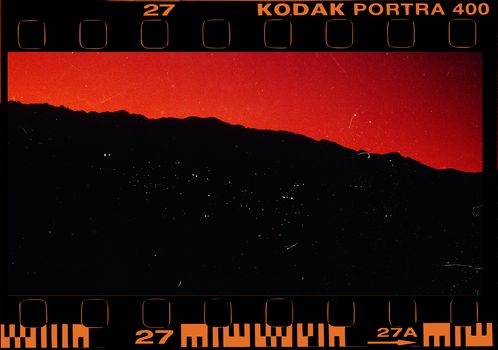 Film-style image of a vibrant red sunset over a silhouette of mountains in Cali, Colombia.