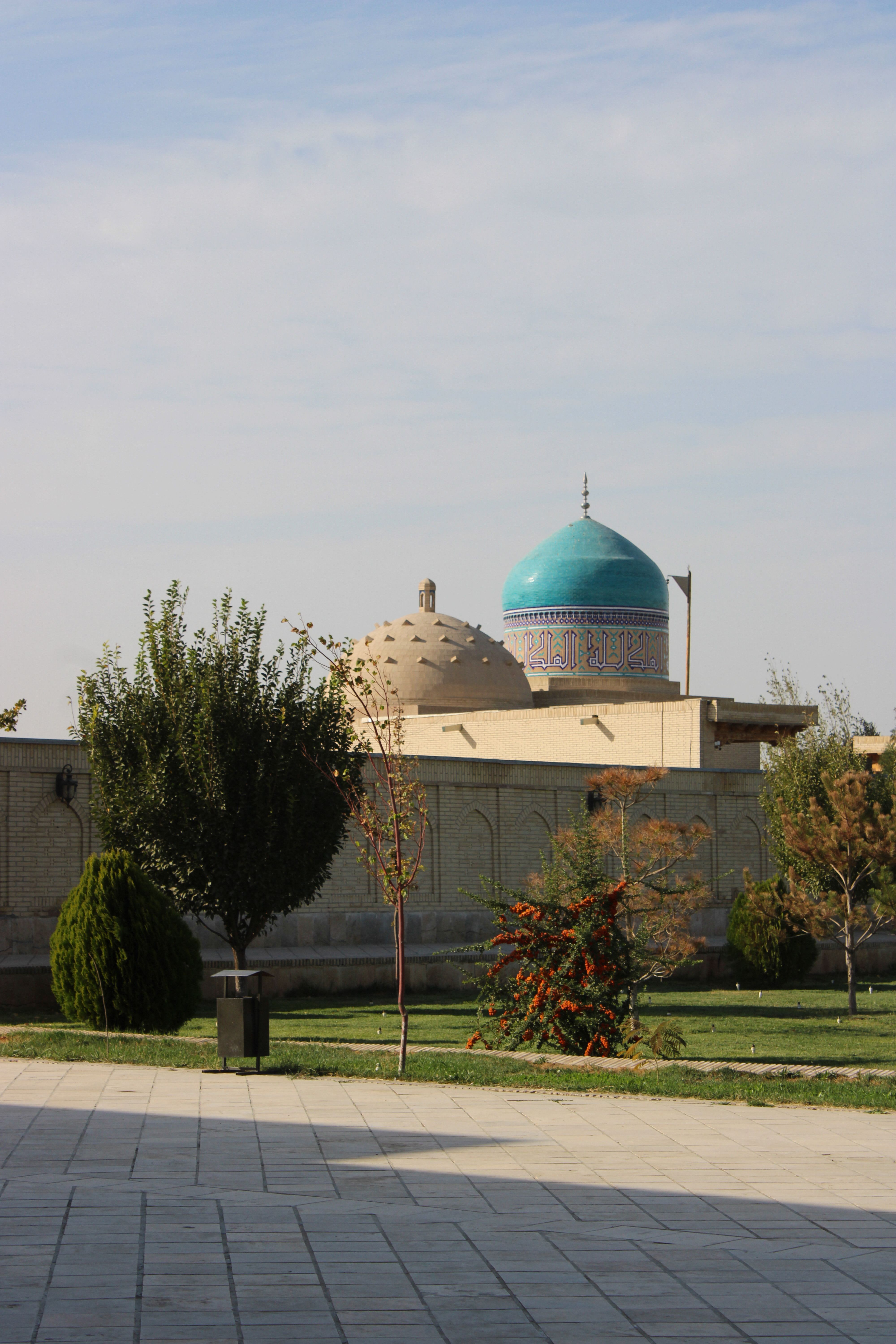 A stunning mosque with a blue dome towers over lush gardens, basking under a clear sky.