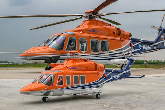 Orange helicopters parked on a concrete helipad in Emden, Germany against a cloudy sky backdrop.
