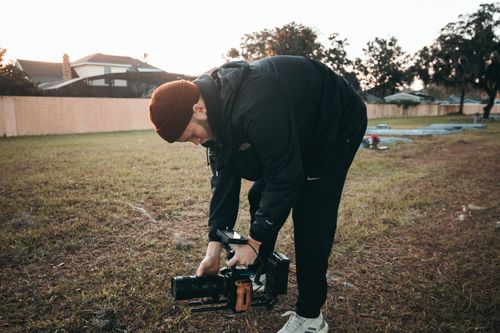 Free A male videographer adjusting his camera equipment during an outdoor shoot at sunrise. Stock Photo