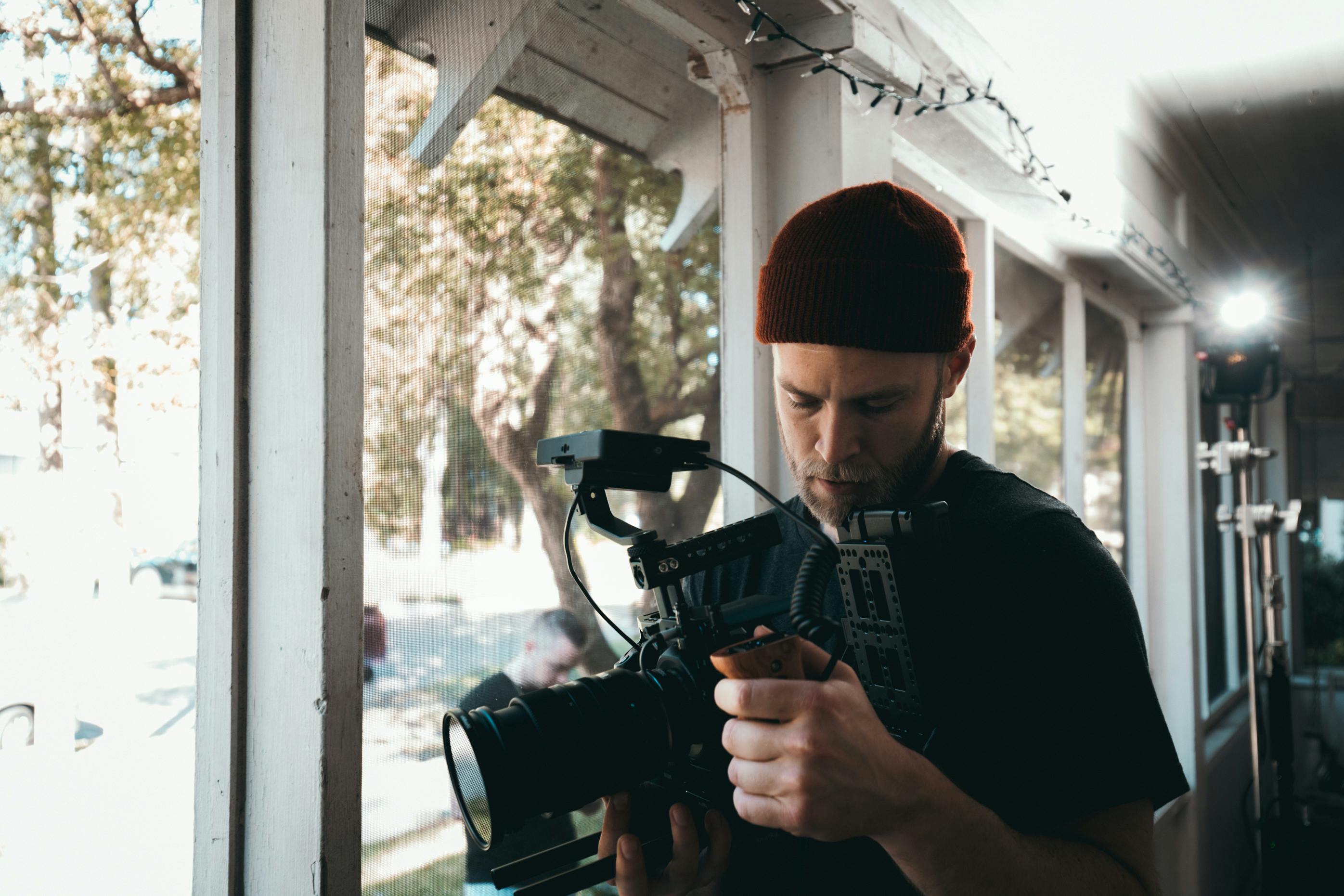 man carrying black video camera standing beside window