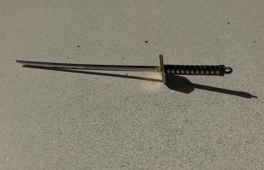 Close-up of a miniature katana sword keychain casting a shadow on a textured surface.
