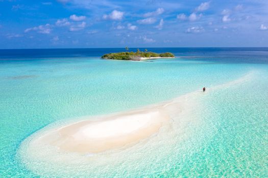 A breathtaking aerial view of a tranquil sandbar leading to a tropical island surrounded by azure waters.