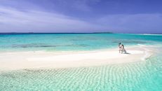 Aerial view of a couple walking on a picturesque sandbar in crystal-clear turquoise waters.