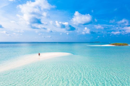 Free Serene aerial view of a tropical island beach with crystal clear blue waters and white sandy shores. Stock Photo