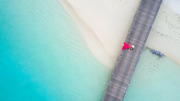 Aerial shot of a woman in a pink dress lying on a beach boardwalk by turquoise waters.