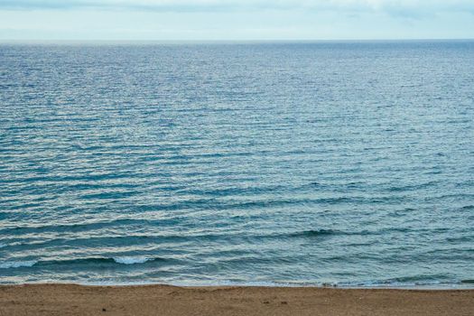 Peaceful view of the ocean waves gently lapping the sandy shore under a calm sky.