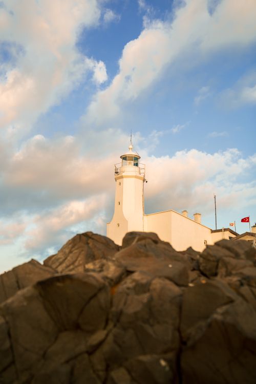 Free A beautiful lighthouse amidst rocky terrain and a dramatic cloudy sky, perfect for travel themes. Stock Photo