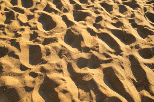 Free Sunlit close-up of textured golden sand on a beach, creating natural patterns and shadows. Stock Photo
