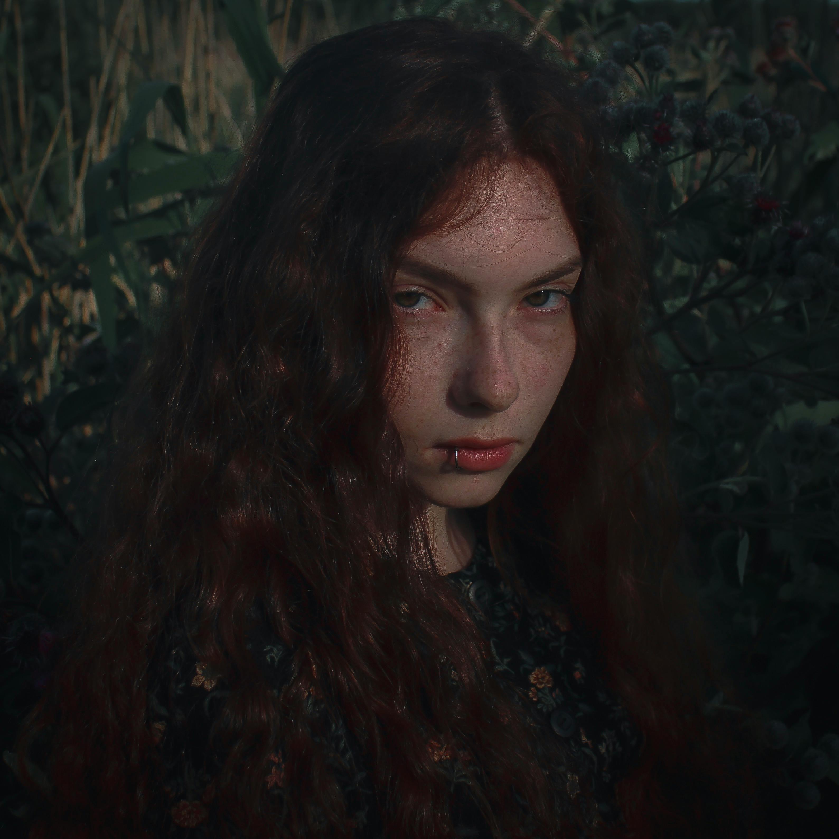 一幅户外拍摄的女人肖像，采用自然光与暗调，营造出戏剧性的阴郁氛围