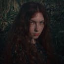 一幅户外拍摄的女人肖像，采用自然光与暗调，营造出戏剧性的阴郁氛围