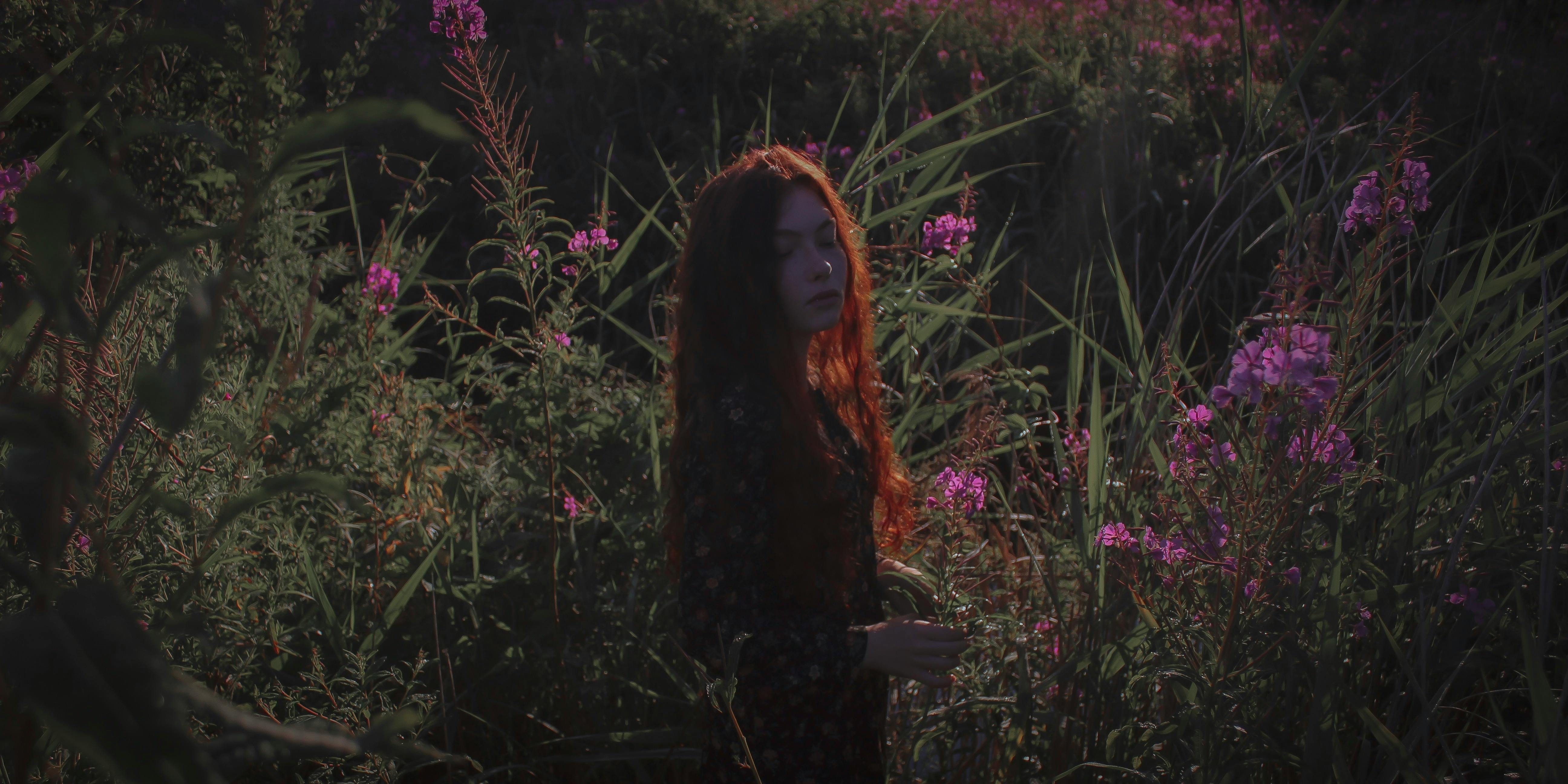 一个红发女人站在宁静的花园里，周围环绕着充满活力的粉红色开花植物