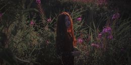 一个红发女人站在宁静的花园里，周围环绕着充满活力的粉红色开花植物