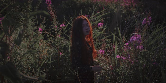 一个红发女人站在宁静的花园里，周围环绕着充满活力的粉红色开花植物