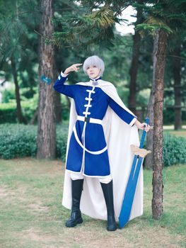 Cosplayer in blue costume with sword posing outdoors in nature.