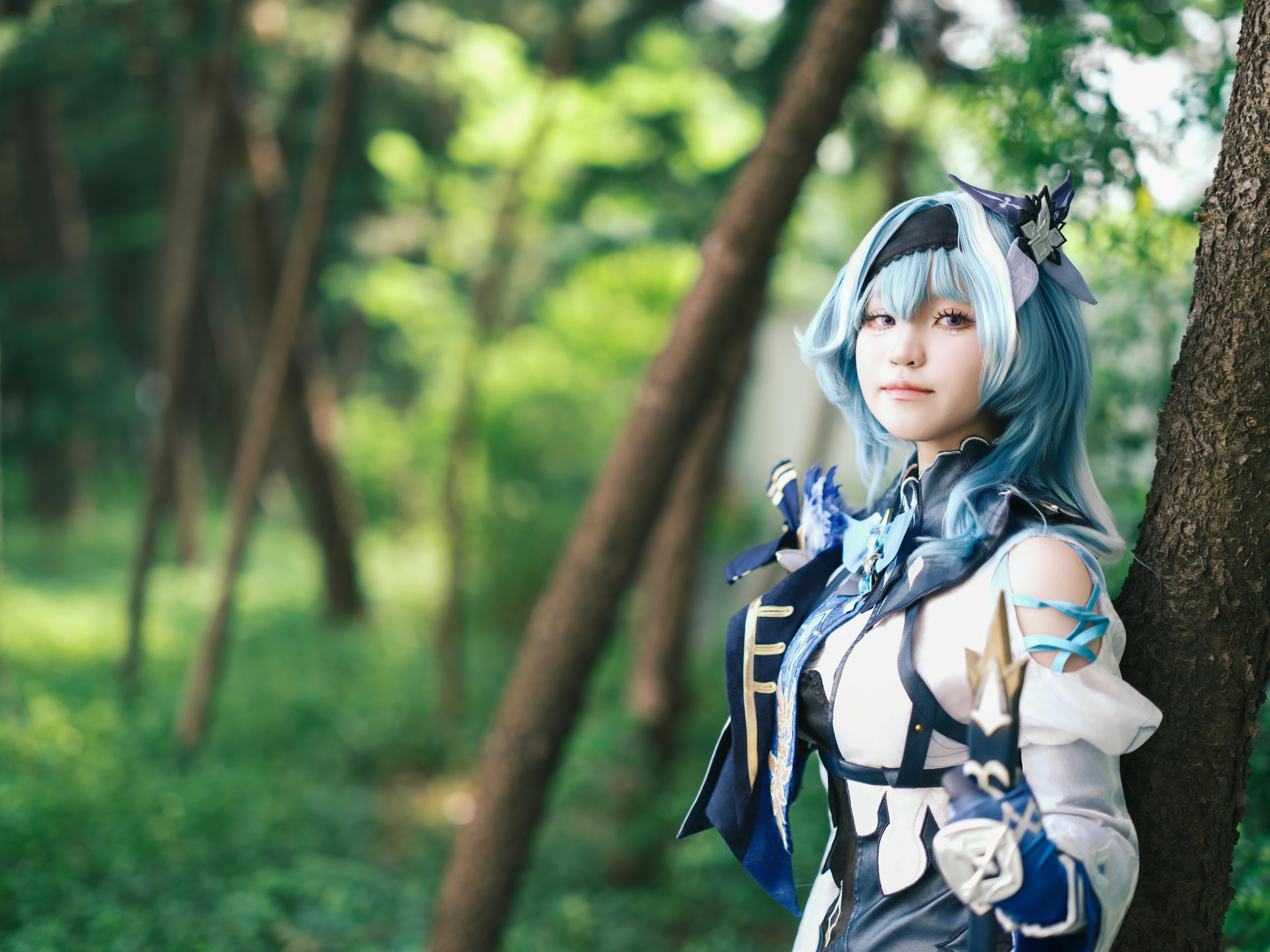 A cosplayer dressed in a blue themed costume poses in a lush forest.