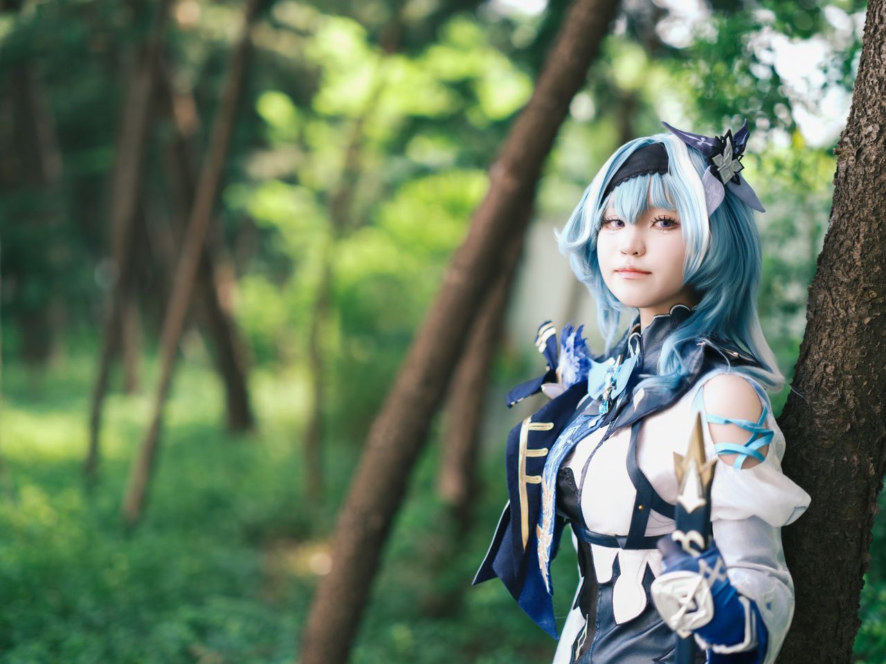 a cosplayer dressed in a blue themed costume poses in a lush forest