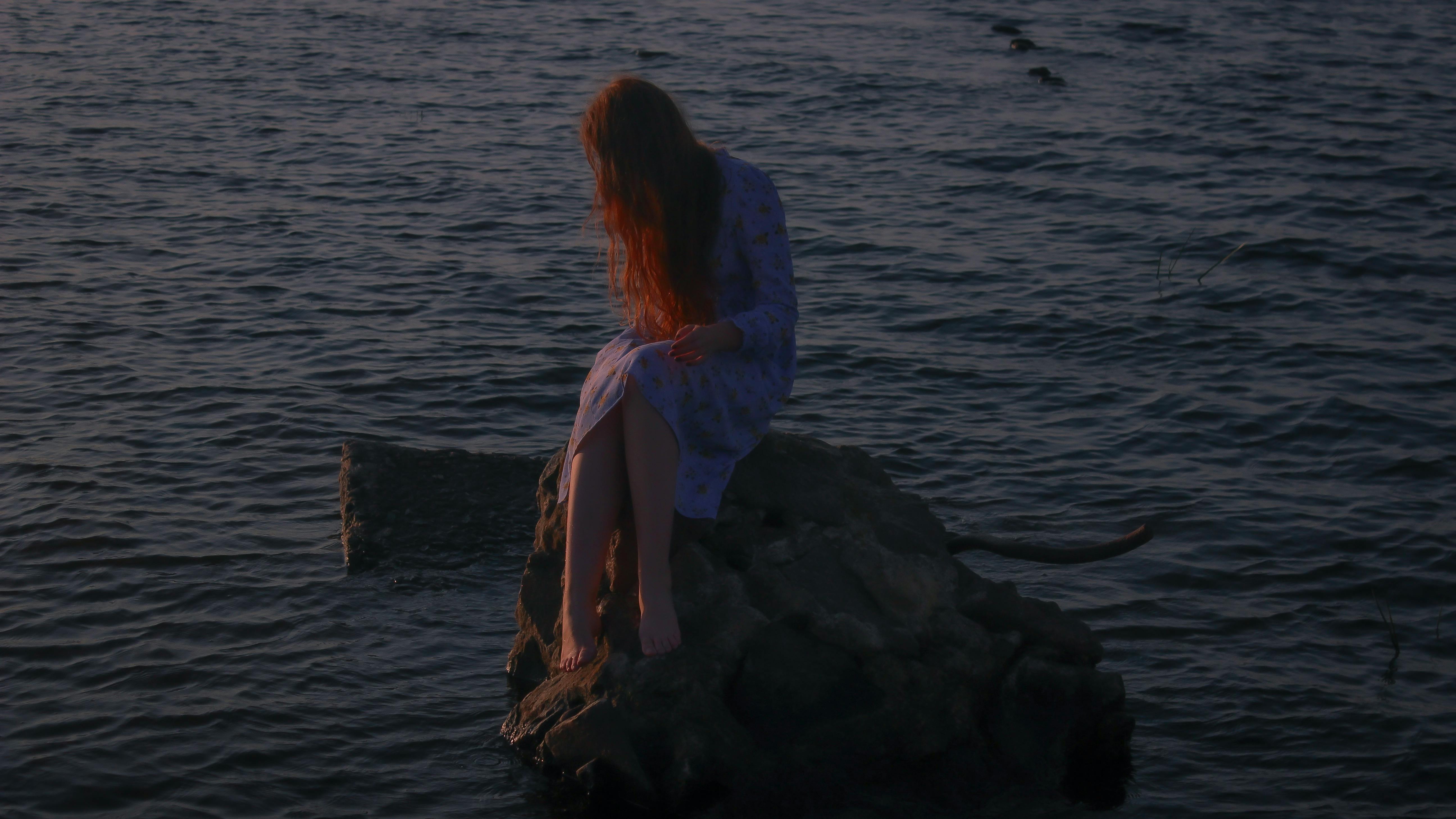 黄昏时分，一个红发女人穿着裙子坐在水边的岩石上