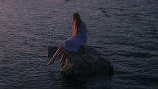 黄昏时分，一个红发女人坐在水边的岩石上