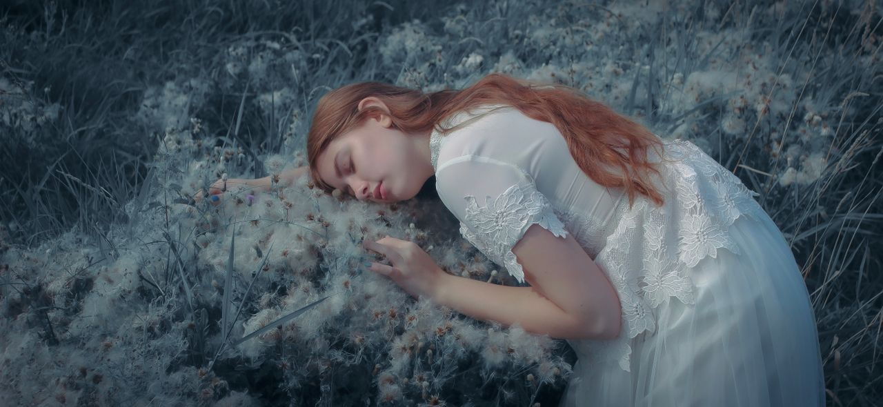 a serene young woman with red hair rests among dandelions outdoors