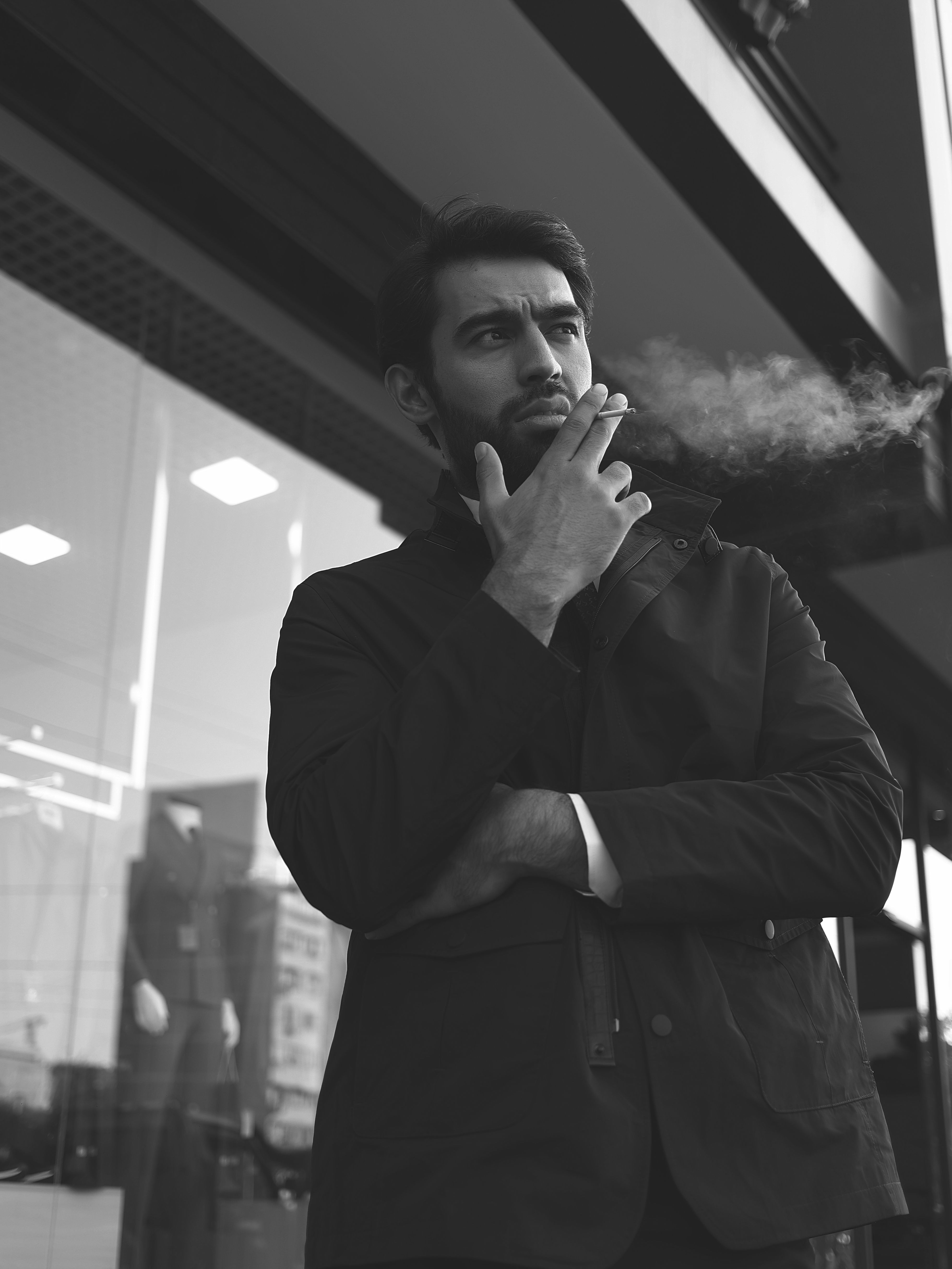 Black and white photo of a man smoking, exuding a pensive mood in a city street setting.
