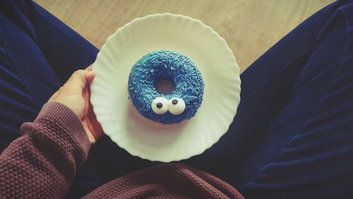 Free A whimsical blue donut with candy eyes and sprinkles on a white plate, held by a person. Stock Photo