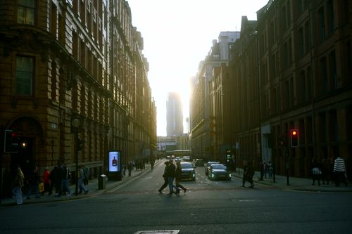 Free City street at sunset with people crossing, cars, and tall buildings. Stock Photo
