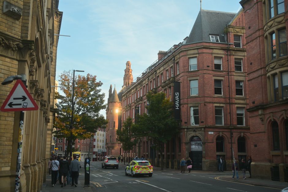 Evening view of a busy street in Manchester with historic brick architecture and people walking.
