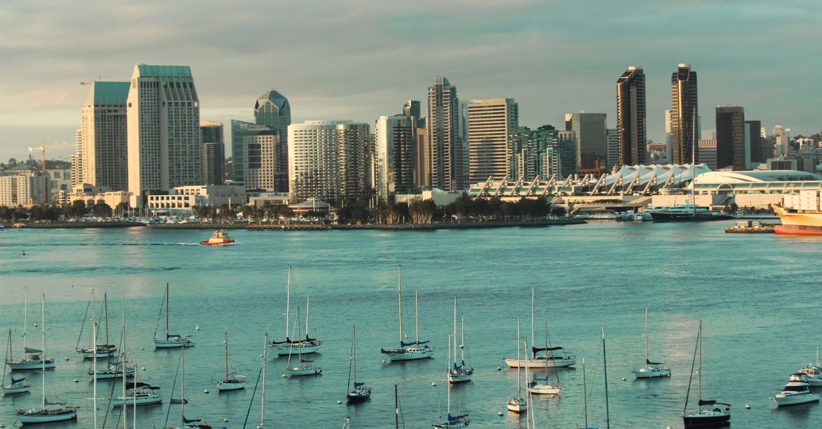 A picturesque view of the San Diego skyline with sailboats anchored in the harbor under a cloudy sky.