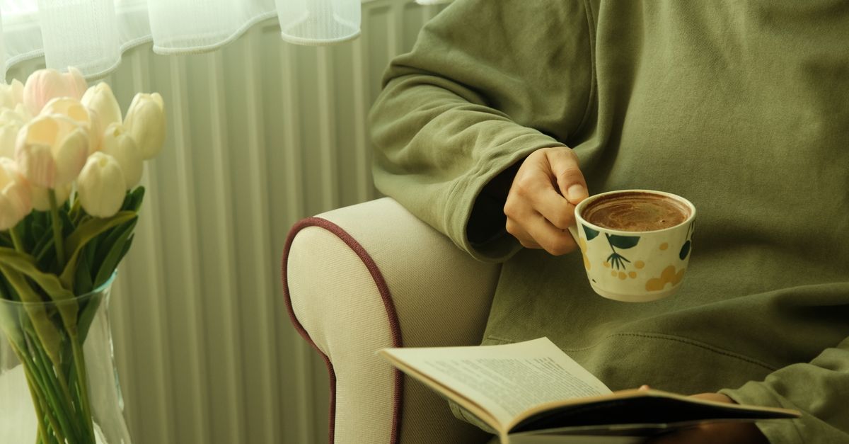 hands holding a book instead of a phone, coffee cup, warm morning light, cozy reading nook