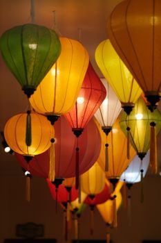 Brightly lit Vietnamese lanterns in vibrant colors hanging indoors.