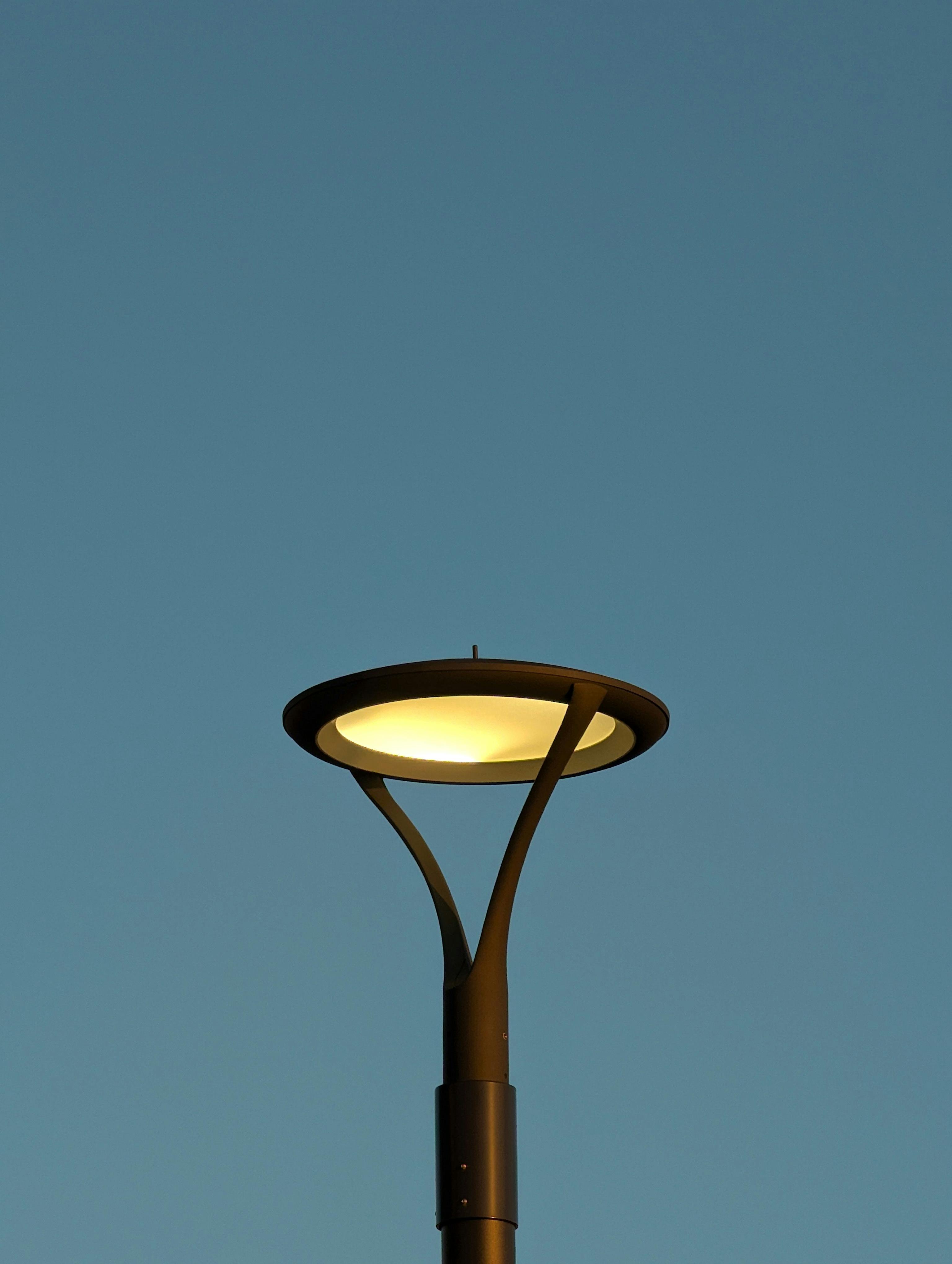 Zadarmo Moderná pouličná lampa teple žiari na pozadí jasnej jesennej večernej oblohy a prezentuje minimalistický dizajn. Fotka z fotobanky