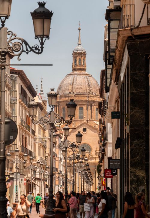 Free Bustling Zaragoza street leading to a historic church dome on a sunny day. Stock Photo