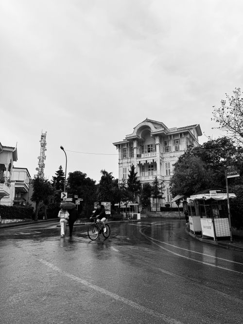 Free Black and white photo of a rainy urban street with historic architecture and people walking and cycling. Stock Photo