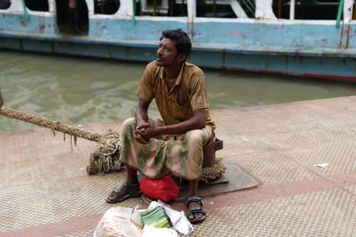 Free A man sitting on a pier by the river in Dhaka, Bangladesh, observing a boat. Stock Photo