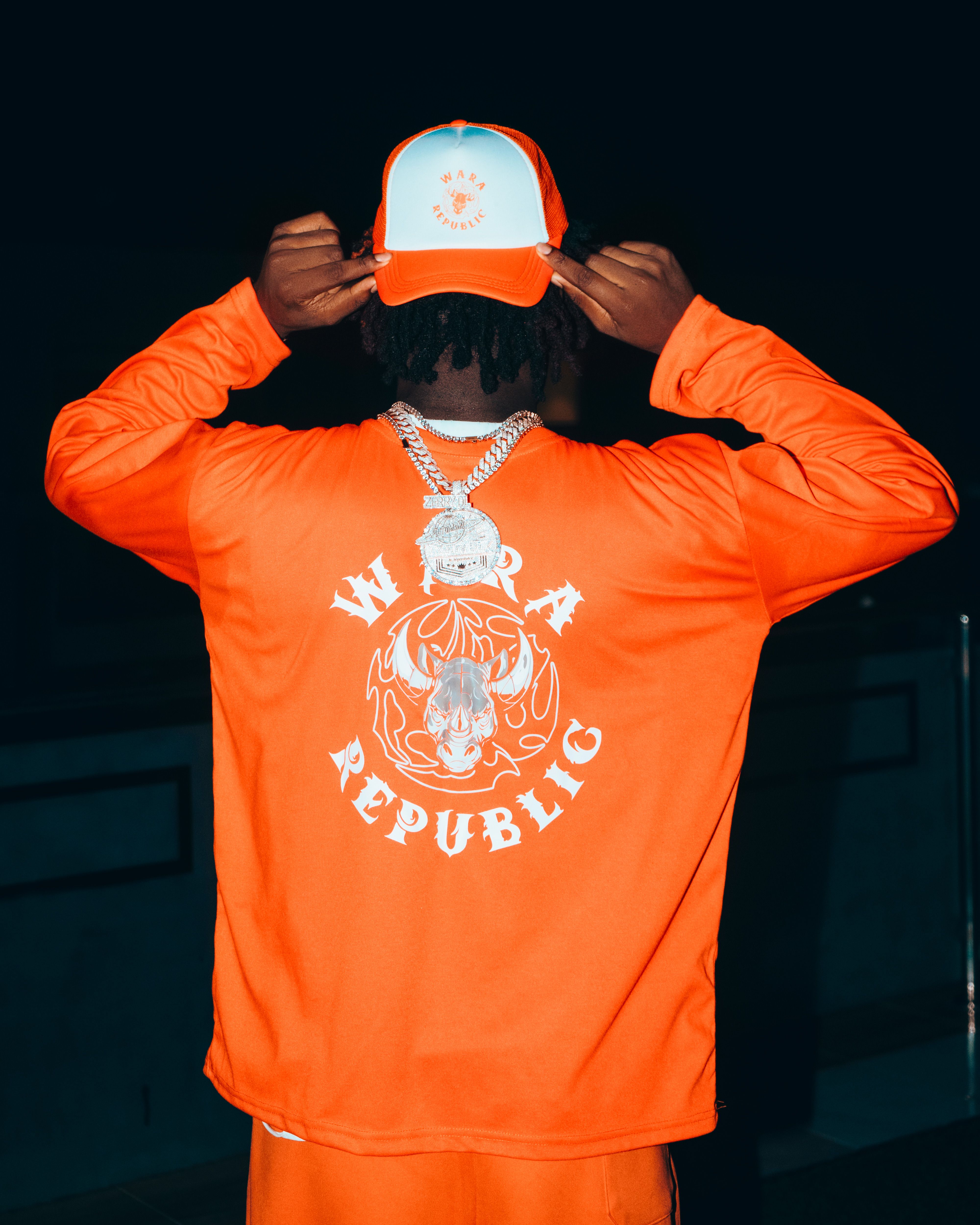 Person showcasing orange streetwear with bold graphic design and chains.