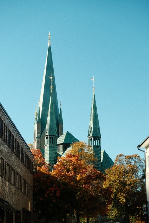 Free A striking view of Nidaros Cathedral with autumn foliage against a clear blue sky. Stock Photo