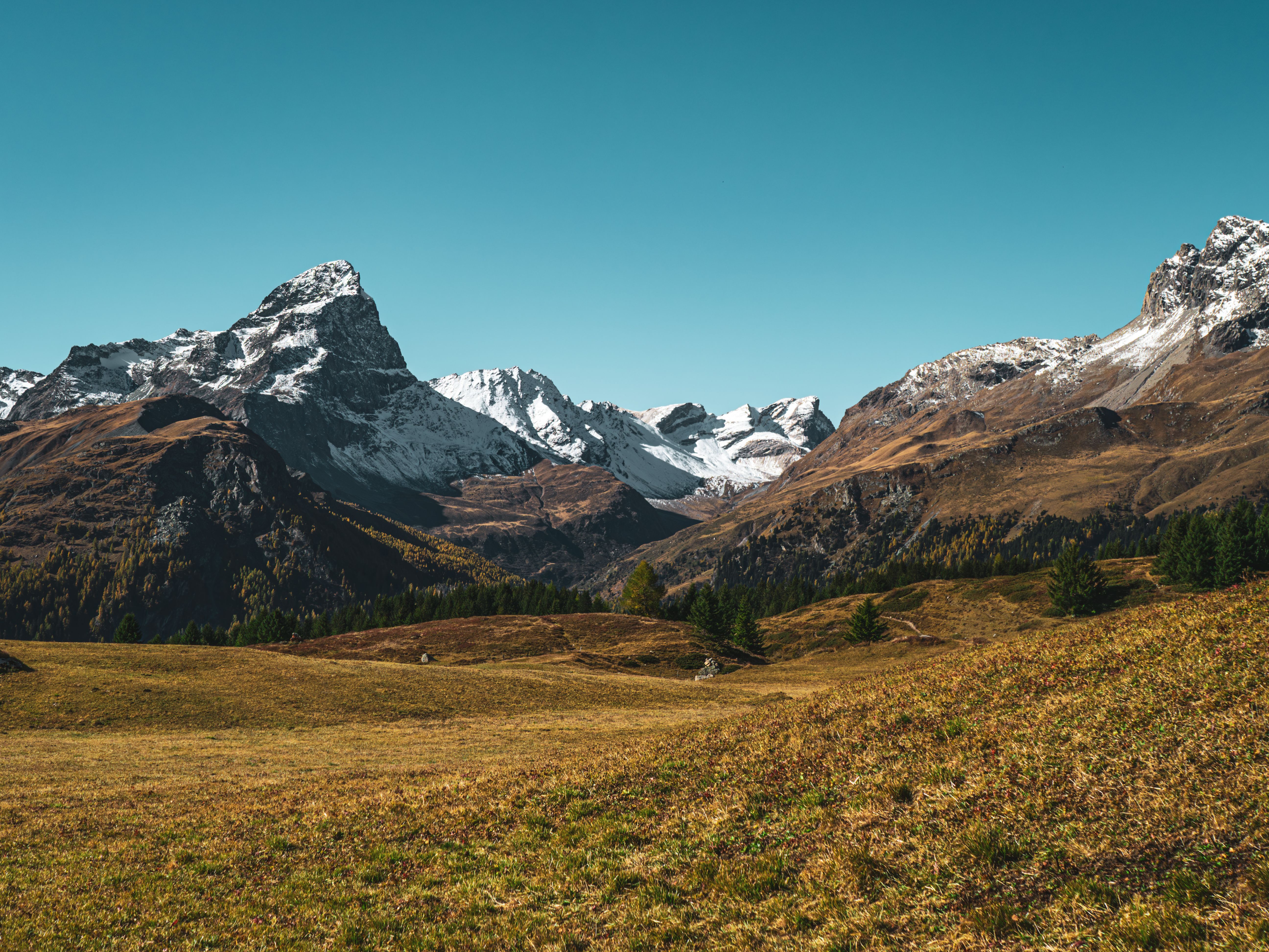 Stunning view of snow-capped peaks in Surses, Graubünden, Switzerland under a clear blue sky.