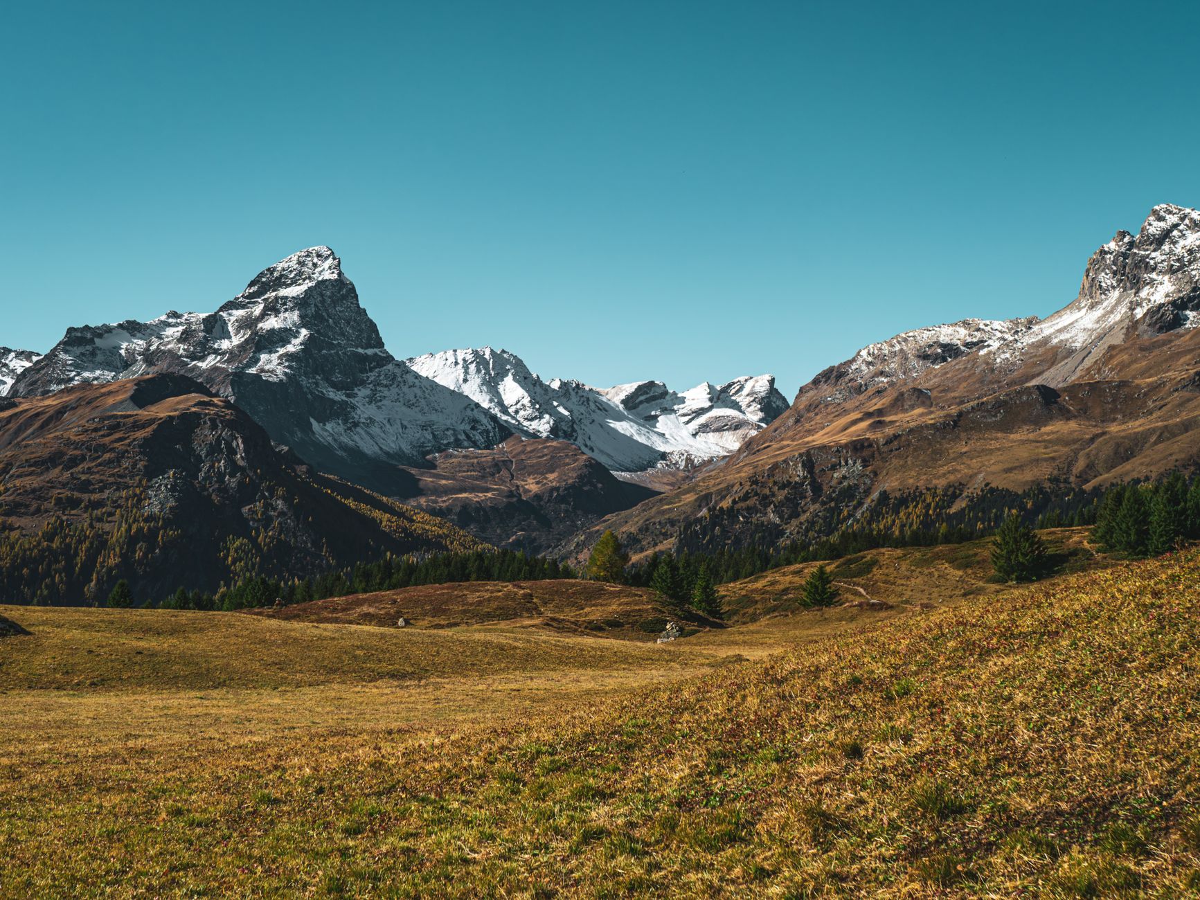 Stunning view of snow-capped peaks in Surses, Graubünden, Switzerland under a clear blue sky.