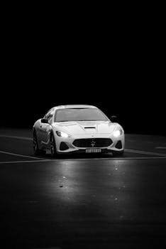 A dramatic black and white photo of a Maserati on an empty street at night, showcasing classic elegance and power.