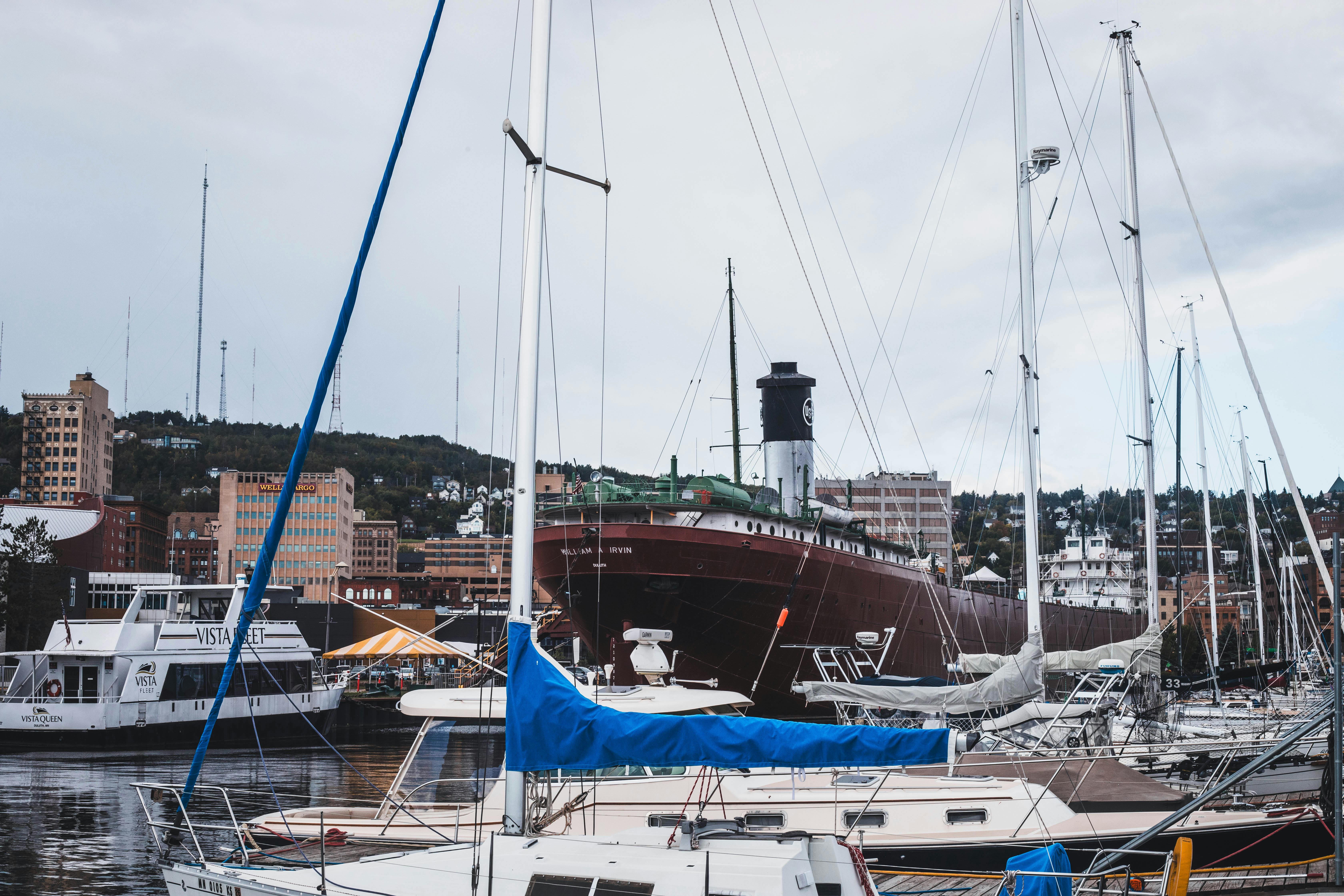 Harbor scene with sailboats moored, city skyline, and overcast sky.