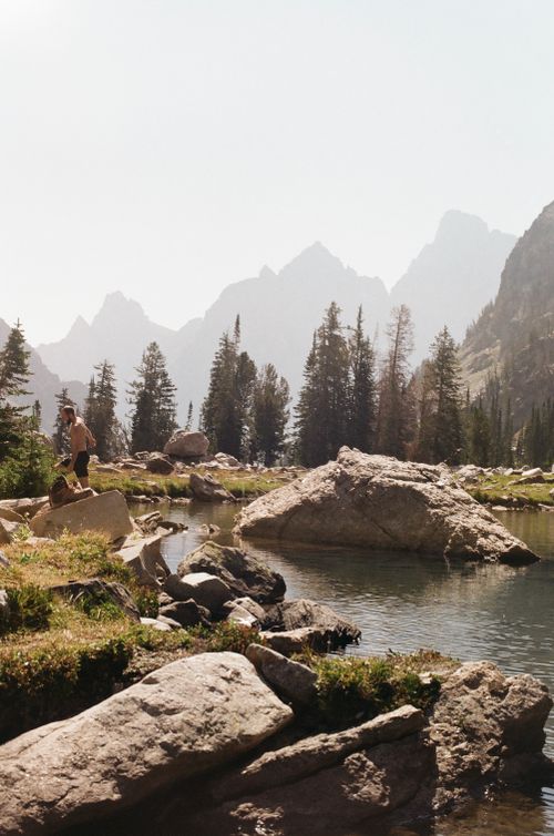 Free Hikers exploring a picturesque mountain lake surrounded by trees and rocks in summer. Stock Photo