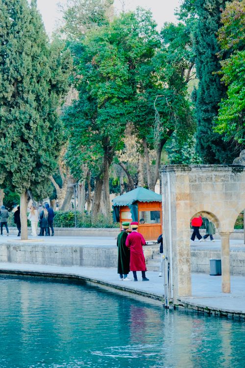 Free People in traditional clothing walking by a serene waterway in a park. Stock Photo